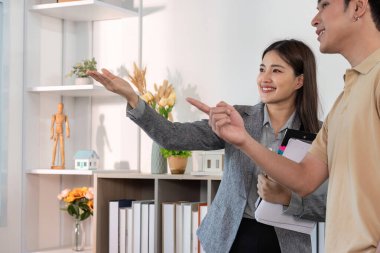 Bir emlakçı, bir mülkü potansiyel bir alıcıya hevesle sunar, özelliklerini gösterir ve sohbete girişir..