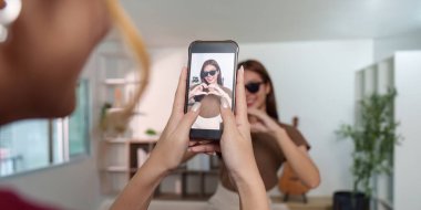 Bir kadın elleriyle kalp şekli oluştururken selfie çeker. Eğlenceli bir atmosferde yaratıcılık ve dostluk sergiler..