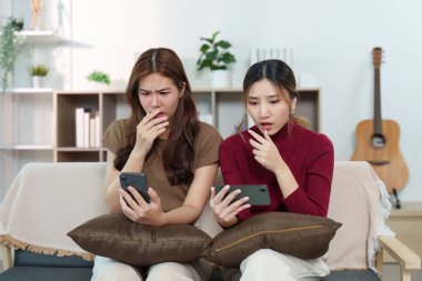 İki genç kadın telefonlarını kontrol ederken şaşkın ve entrika dolu bir anı yakalarken şaşırmış yüz ifadeleri sergilerler..