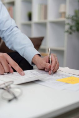 Odaklanmış bir birey vergi formlarını gözden geçirir ve mali konulardaki doğruluğun önemini vurgulayarak hesaplamalar yapar..