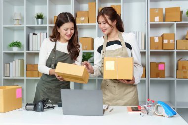 Bir e-ticaret ofisinde işbirliği yapan, paketleri yöneten ve sipariş için dizüstü bilgisayar kullanan iki kadın..