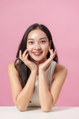 Yüzünde parlak bir gülümsemeyle poz veren genç bir kadın, pembe bir arkaplana karşı güzellik ve özgüven vurguluyor..