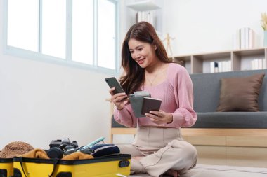 Bir kadın sevinçle seyahat planlarını düzenliyor, telefonunu kullanıyor ve pasaportunu kapalı bir yerde tutuyor..