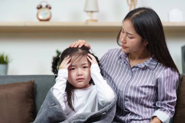 Bir anne hasta kızını nazikçe rahatlatır. Hastalık anında sevgi ve destek gösterir. Rahat bir evde..