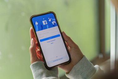 CHIANG MAI ,THAILAND - Oct 17, 2025 : Woman hand holding iPhone to use facebook with new login screen Facebook is a largest social network and most popular social networking site in the world.