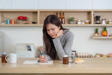 Sağlık gereksinimleriyle çevrili bir şekilde bir günlüğe yazan bir kadın, sabah rutinini vurguluyor..
