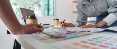 Mimarlar, modern bir çalışma alanında renk örnekleri ve bir dizüstü bilgisayar kullanarak tasarım projelerine odaklanırlar..