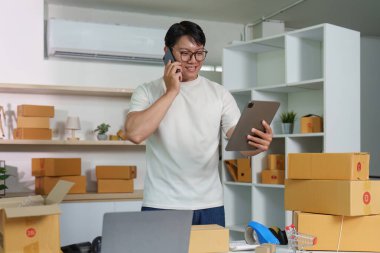 Gülümseyen bir adam, modern bir ofis ortamında tabletinin detaylarını kontrol ederken telefonda konuşur..