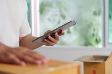 Bir birey, iş faaliyetlerindeki dijital dönüşümü vurgulayarak, çağdaş bir çalışma alanında envanteri izlemek için bir tablet kullanır.