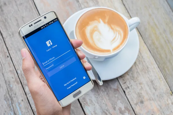 Een hand van de man met screen shot van facebook. Facebook is een online dienst van sociale media voor microblogging en netwerken. — Stockfoto