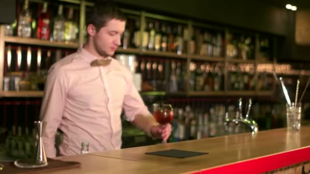 Welcome to our bar. Handsome bartender in a bow tie putting a cocktail on a bar table smiling happily camera sliding — Αρχείο Βίντεο