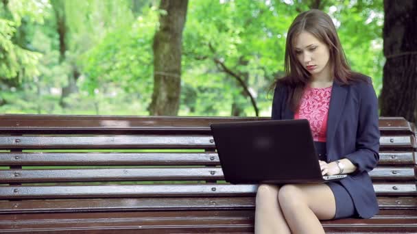 Молодая деловая женщина с ноутбуком работает. Скамейка в парке — стоковое видео