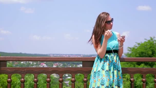 난간 근처 헤드폰을 통해 매력적인 소녀 청취 음악. 중간 — 비디오