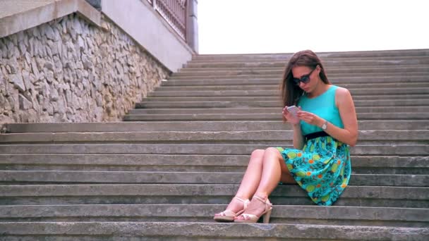 Chica atractiva escribiendo texto en el teléfono sentado en escaleras viejas. Ángulo ancho — Vídeo de stock