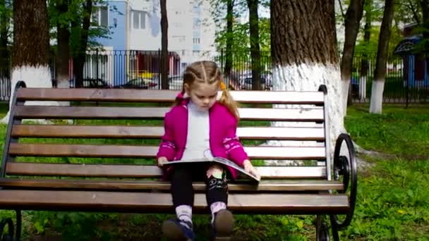 Mädchen liest ein Buch, während sie auf der Bank sitzt Schieberegler schiebt — Stockvideo