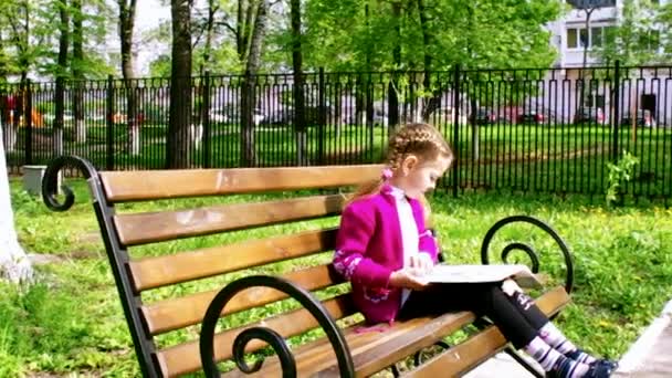 Chica leyendo un libro mientras está sentado en el banco — Vídeo de stock