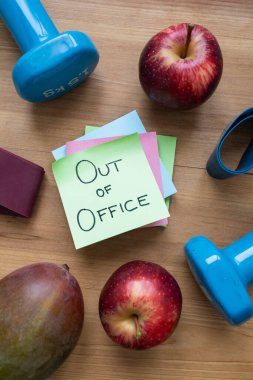Green Out of Office Sticky Note Surrounded by Fruit and Fitness Accessories