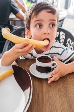 Çocuk bir fincan kalın sıcak çikolatayla çerez yiyor.