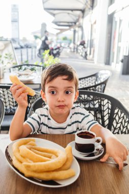 Çocuk bir fincan kalın sıcak çikolatayla çerez yiyor.