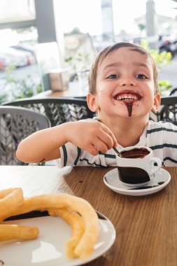 Gülümseyen çocuk bir fincan sıcak çikolatanın tadını çıkarıyor..