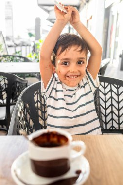 Bir fincan sıcak çikolatanın tadını çıkardıktan sonra çikolata lekeli yüzü olan neşeli küçük çocuk..