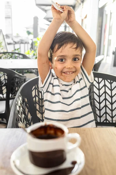 Bir fincan sıcak çikolatanın tadını çıkardıktan sonra çikolata lekeli yüzü olan neşeli küçük çocuk..