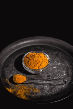 Zıt bir arkaplan üzerinde koyu bir tabakta servis edilen altın zerdeçal tozu.