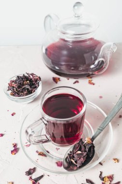 Kurumuş amber yaprağının yanına yerleştirilmiş canlı kırmızı bir çay fincanı bu bitkisel karışımın tazeliğini, rengini ve doğal güzelliğini vurgular..