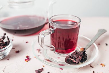 Kurumuş amber yaprağının yanına yerleştirilmiş canlı kırmızı bir çay fincanı bu bitkisel karışımın tazeliğini, rengini ve doğal güzelliğini vurgular..