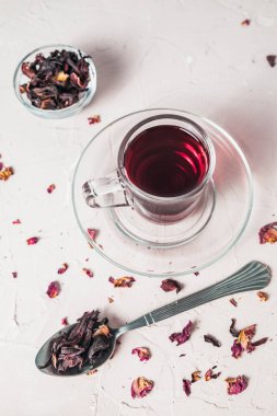 Kurumuş amber yaprağının yanına yerleştirilmiş canlı kırmızı bir çay fincanı bu bitkisel karışımın tazeliğini, rengini ve doğal güzelliğini vurgular..