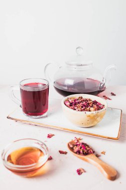 Kurumuş amber yaprağının yanına yerleştirilmiş canlı kırmızı bir çay fincanı bu bitkisel karışımın tazeliğini, rengini ve doğal güzelliğini vurgular..