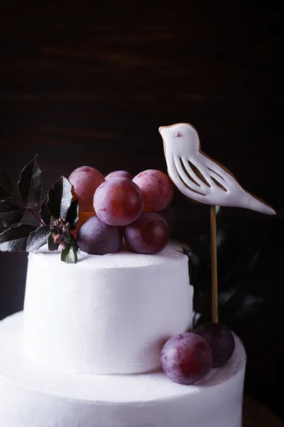 Biały tort dwu warstwowych z winogron ptak i pozostawia na ciemnym tle drewniane z ciemności światło — Zdjęcie stockowe