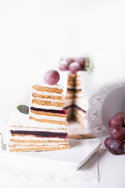 Cut cake souffle on a white background with white decor and grapes — Stock Photo, Image