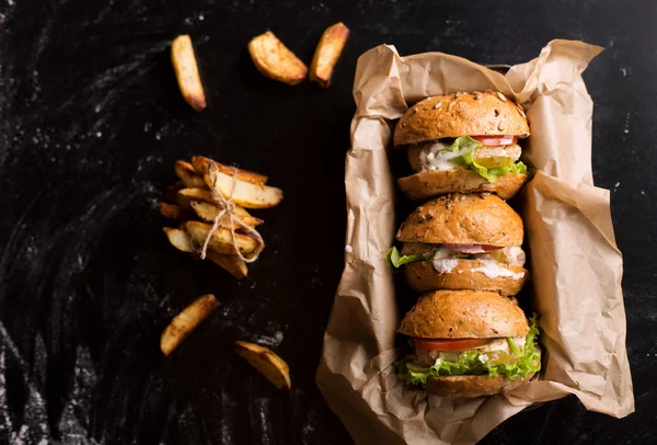 Yukarıdaki üç hamburger patates rustik, ile tekne içinde karanlık bir arka plan üzerinde göster