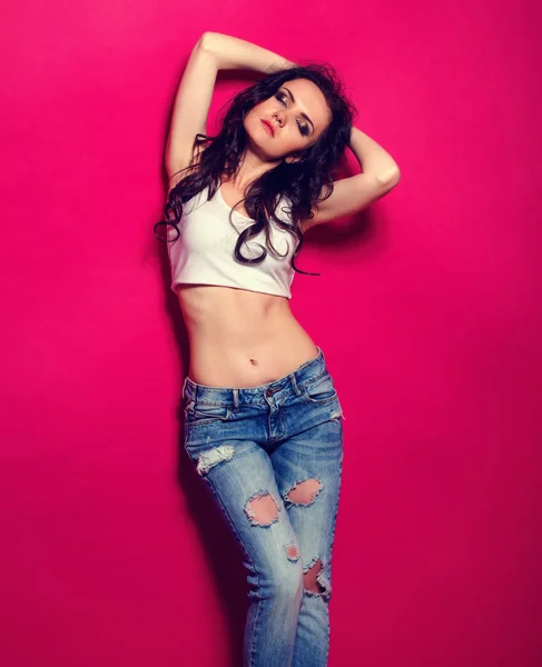 Stylish slim girl in the jeans and bra in the studio on the pink background — Stock Photo, Image