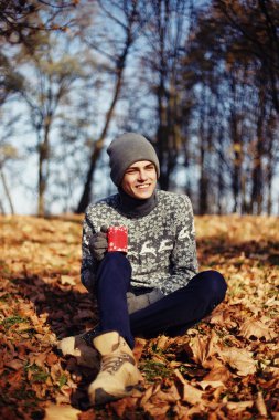 Şık mutlu yakışıklı genç kazak ve fincan çay ya da kahve sonbahar Park ile şapka