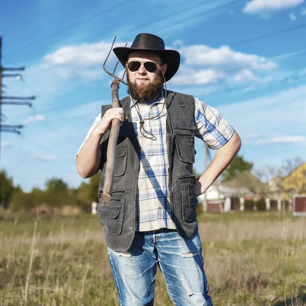 Farmer in the hat and sunglasses with the pitchfork outdoor — Stock Photo, Image