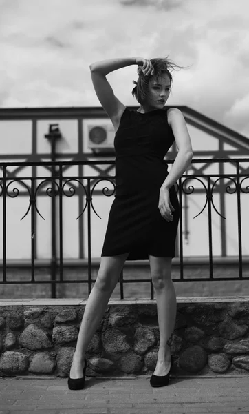 Vogue model in the black dress outdoor near fence