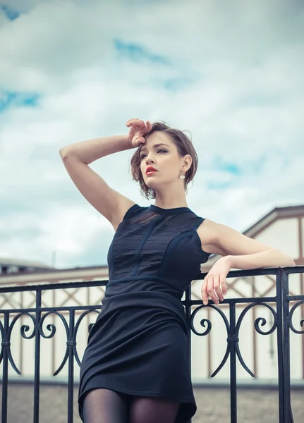 Модель Vogue в чорній сукні на відкритому повітрі біля паркану — стокове фото