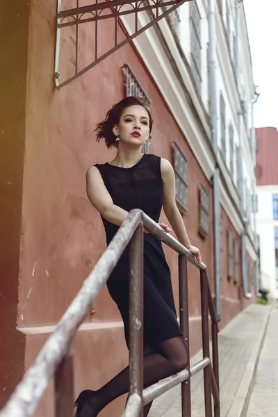 Модель Vogue в чорній сукні на відкритому повітрі біля будівлі біля паркану — стокове фото