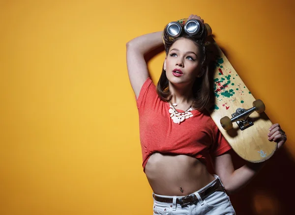 Красивая модная девушка со скейтбордом перед желтым — стоковое фото
