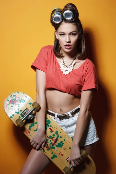 Krásná módní dívka s skateboard před žlutá — Stock fotografie