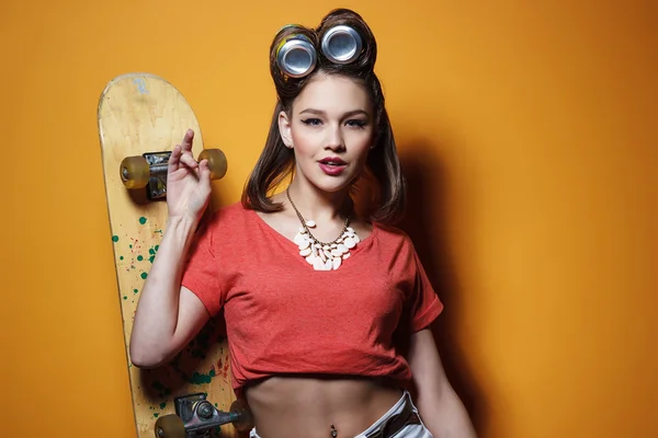 Bella ragazza alla moda con uno skateboard davanti a sfondo giallo — Foto Stock