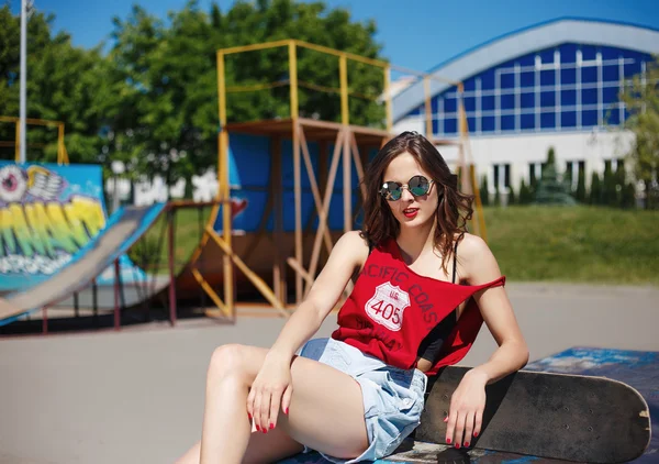 Hipster ragazza in jeans e occhiali da sole con skateboard all'aperto — Foto Stock