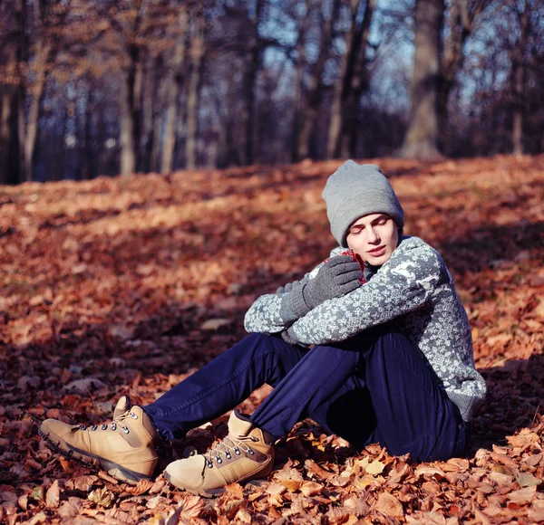 Bello elegante felice giovane nel maglione e cappello con la tazza di tè o caffè nel parco autunnale — Foto Stock