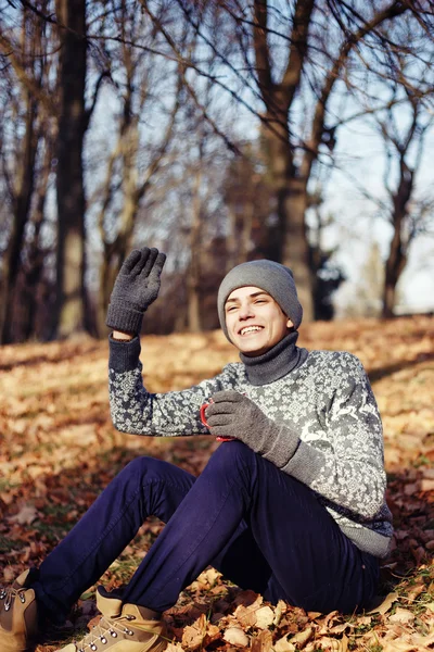 Гарний стильний щасливий молодий чоловік в светрі і капелюсі з чашкою чаю або кави в осінньому парку — стокове фото