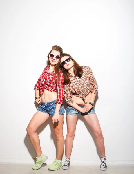 Close up fashion lifestyle portrait of two young hipster girls best friends, wearing bright make up and trendy clothes, making funny faces and have gray time. Urban  background. — Stock Photo, Image