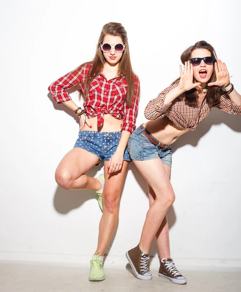 Nahaufnahme Mode-Lifestyle-Porträt zweier junger Hipster-Mädchen beste Freunde, tragen helle Make-up und trendige Kleidung, machen lustige Gesichter und haben graue Zeit. Urbaner Hintergrund. — Stockfoto