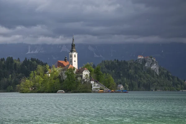 Lac de Bled et église de pèlerinage ensoleillé avec fond sombre — Photo