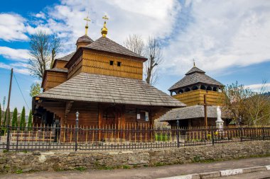 Historic Church of the Great Martyr Panteleimon, a beautiful example of traditional wooden Carpathian architecture in Skole, Ukraine, featuring intricate roofs and golden domes under a blue sky